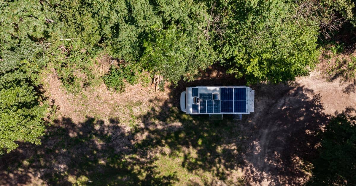Flygvy av en campervan med takmonterade solpaneler parkerad i en skogsglänta