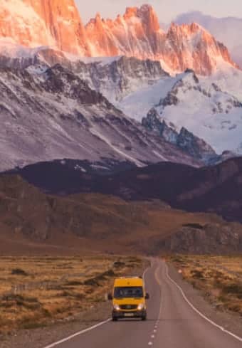 Gul campingbuss på en öppen väg nedanför det snöklädda Fitz Roy-massivet i Patagonien